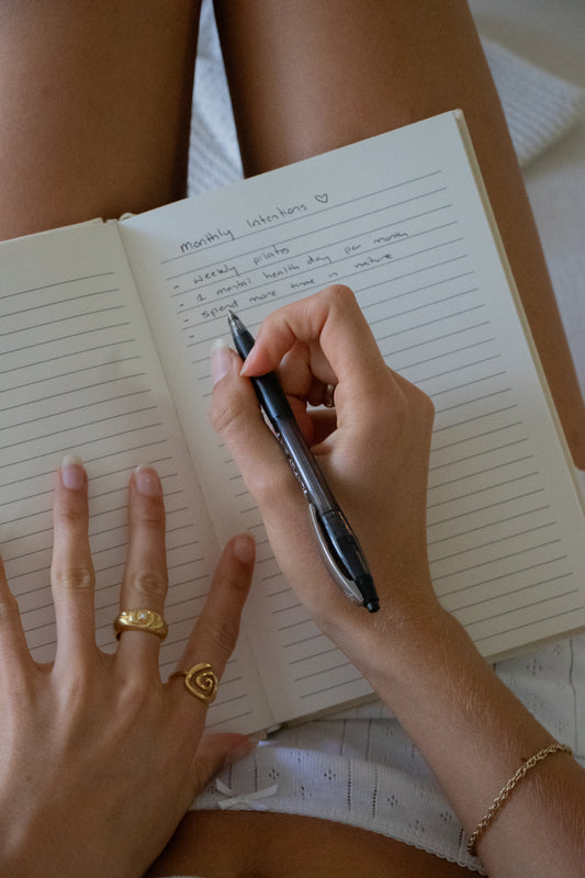 Person writing in a notebook with a pen, wearing rings and a bracelet.