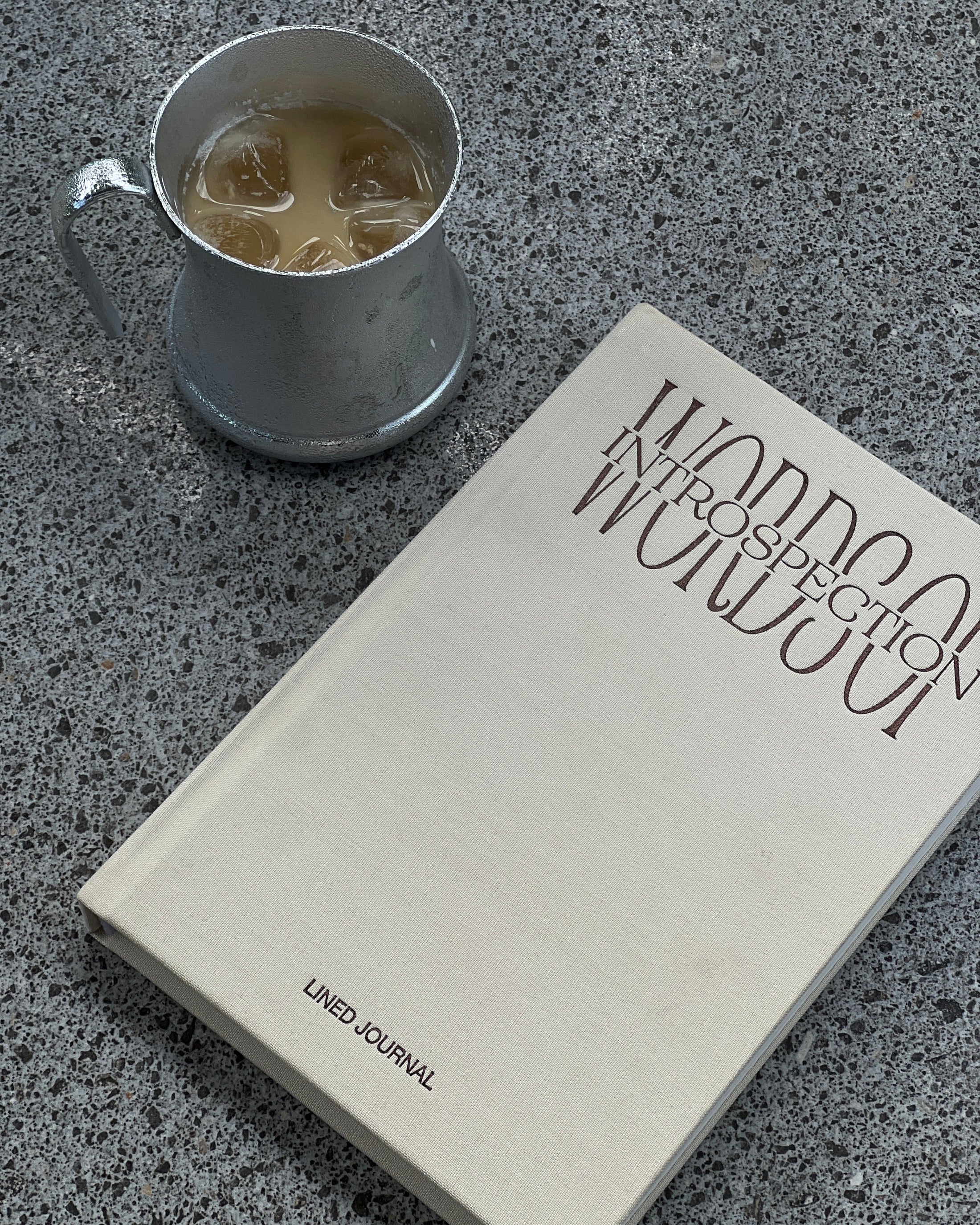 Lined Journal with text on a concrete surface next to a metal cup with a coffee.